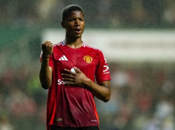 Um jogador de futebol com uma camisa vermelha com a mão no peito e o punho levantado.