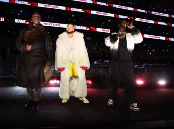 Três homens no palco com "Eubank Jr. Próxima geração" exibido em telas em segundo plano.