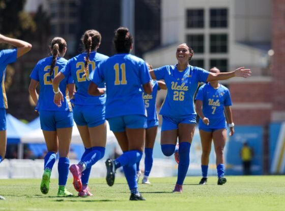 Meila Brewer estende os braços, sorri e corre para abraçar seus companheiros da UCLA durante uma partida contra Stanford.